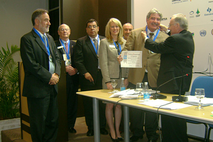 Engineer Miguel Ángel Yadarola, president of API (to the right) places the medal that grants their members their titles around Bengamín Colucci’s neck.