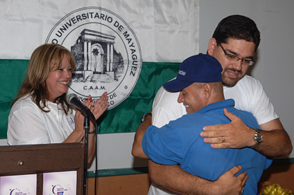 El decano de Administración, licenciado José A. Frontera abraza a Ángel Cintrón, padrino del evento que se llevará a cabo en el RUM. Observa Lourdes Ayala.