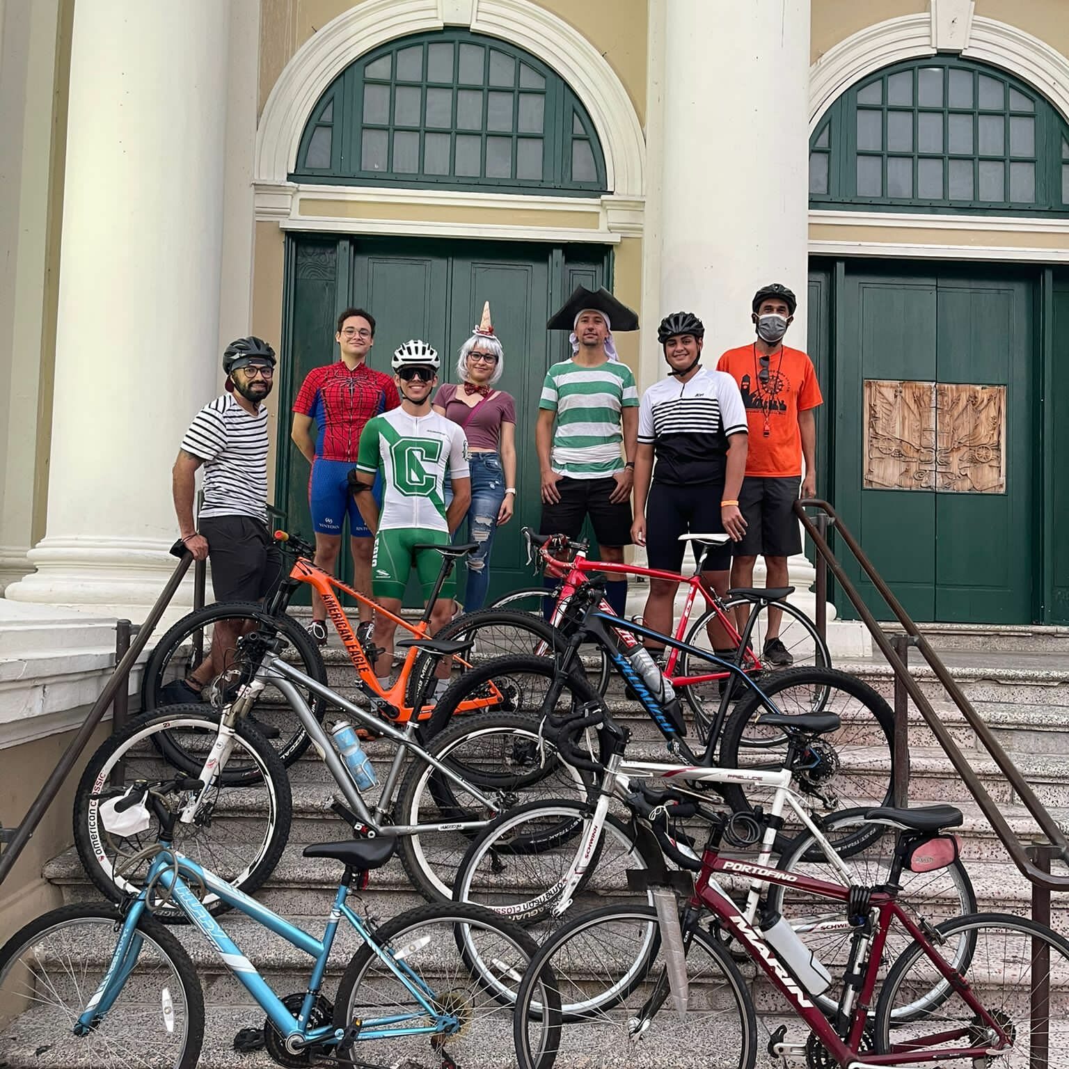 Ciclistas en segundo plano, algunos disfrazados con motivo de halloween y sus bicicletas en primer plano en las escaleras frente a la Casa Alcaldía de Mayagüez.