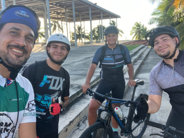 Ciclistas participantes de la Organización Estudiantil Ride a Bike del RUM en una vuelta recreativa al atardecer con la Plaza de las Banderas en EL Litoral de fondo.