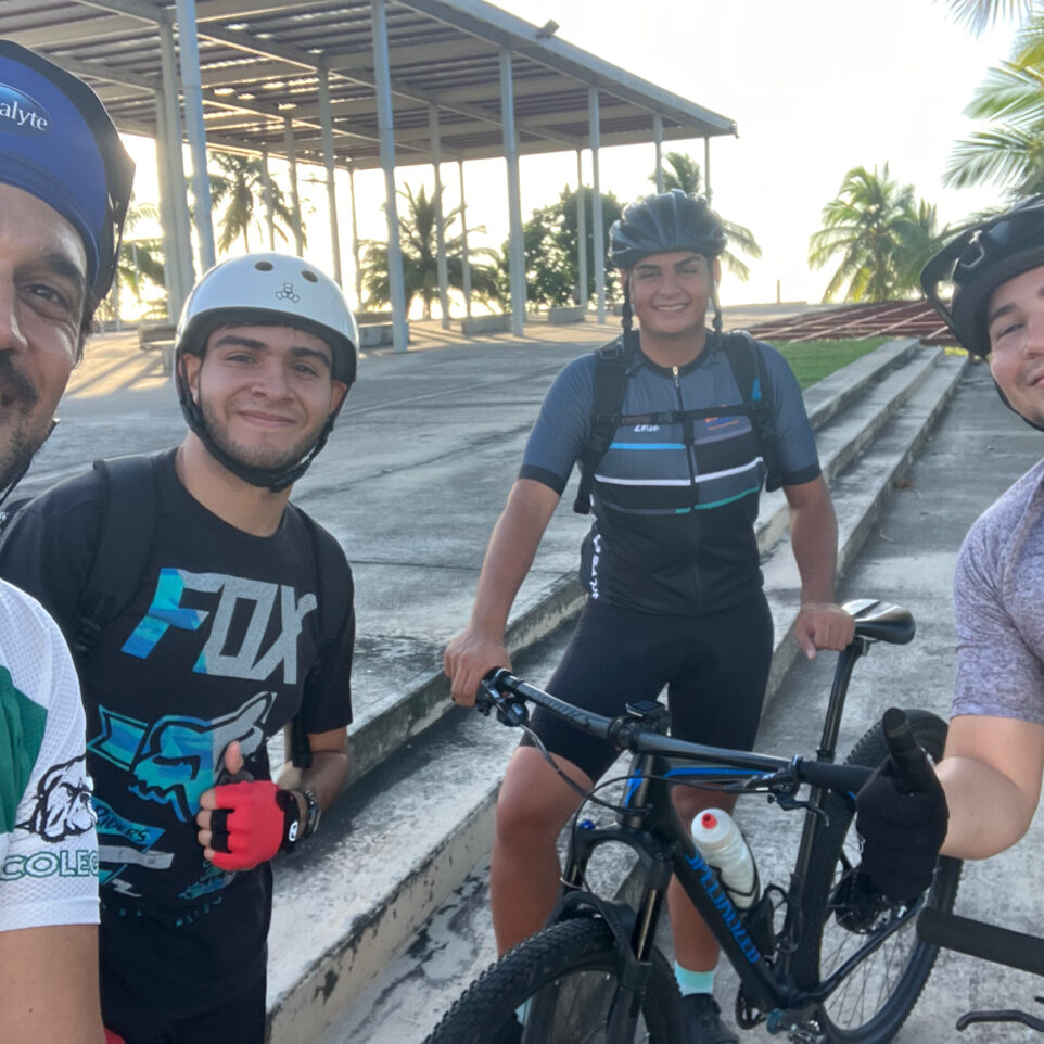 Ciclistas participantes de la Organización Estudiantil Ride a Bike del RUM en una vuelta recreativa al atardecer con la Plaza de las Banderas en EL Litoral de fondo.