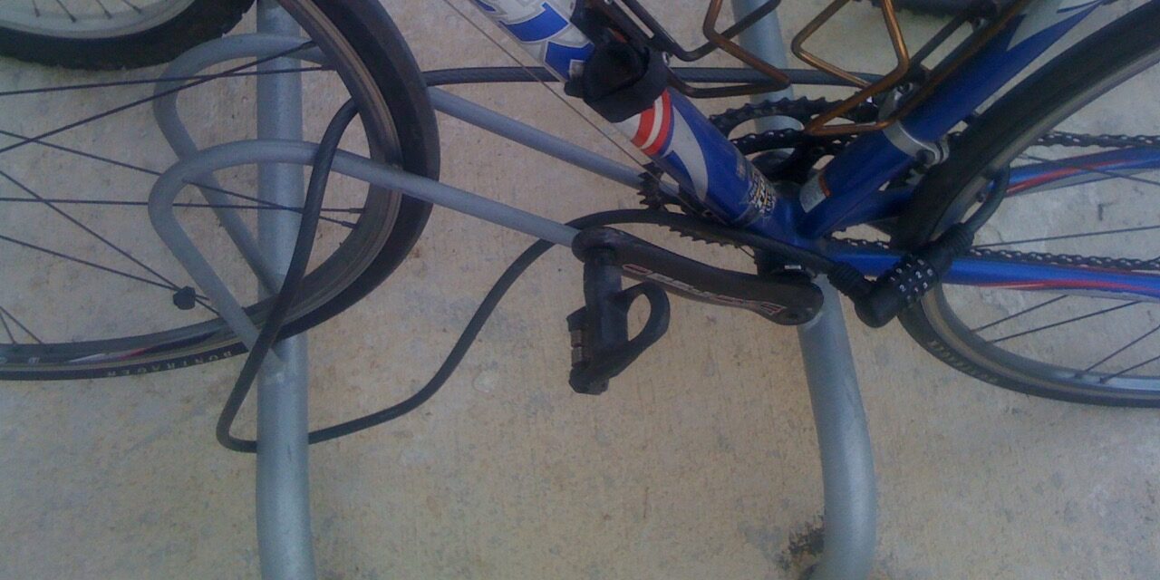 Bicicleta asegurada con un cable de combinación a una percha fija en el suelo.