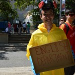 A student in a hazmat suit holding a hand made sign that says English Department as means of promotion for the Open House.