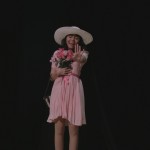 Cast member for the student presented play of The Rocky Horror Picture show on stage holding her hand out and holding flowers.