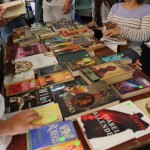 A closer look at all of the books on top of the second table of the EDSA Book & Bake Sale. Some customers are looking at the pages of a book.