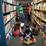 Children sitting on the floor looking at two EDSA members in a library hallway.