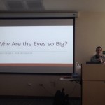 A student giving a presentation from the podium. To the left is the screen with the material being projected.