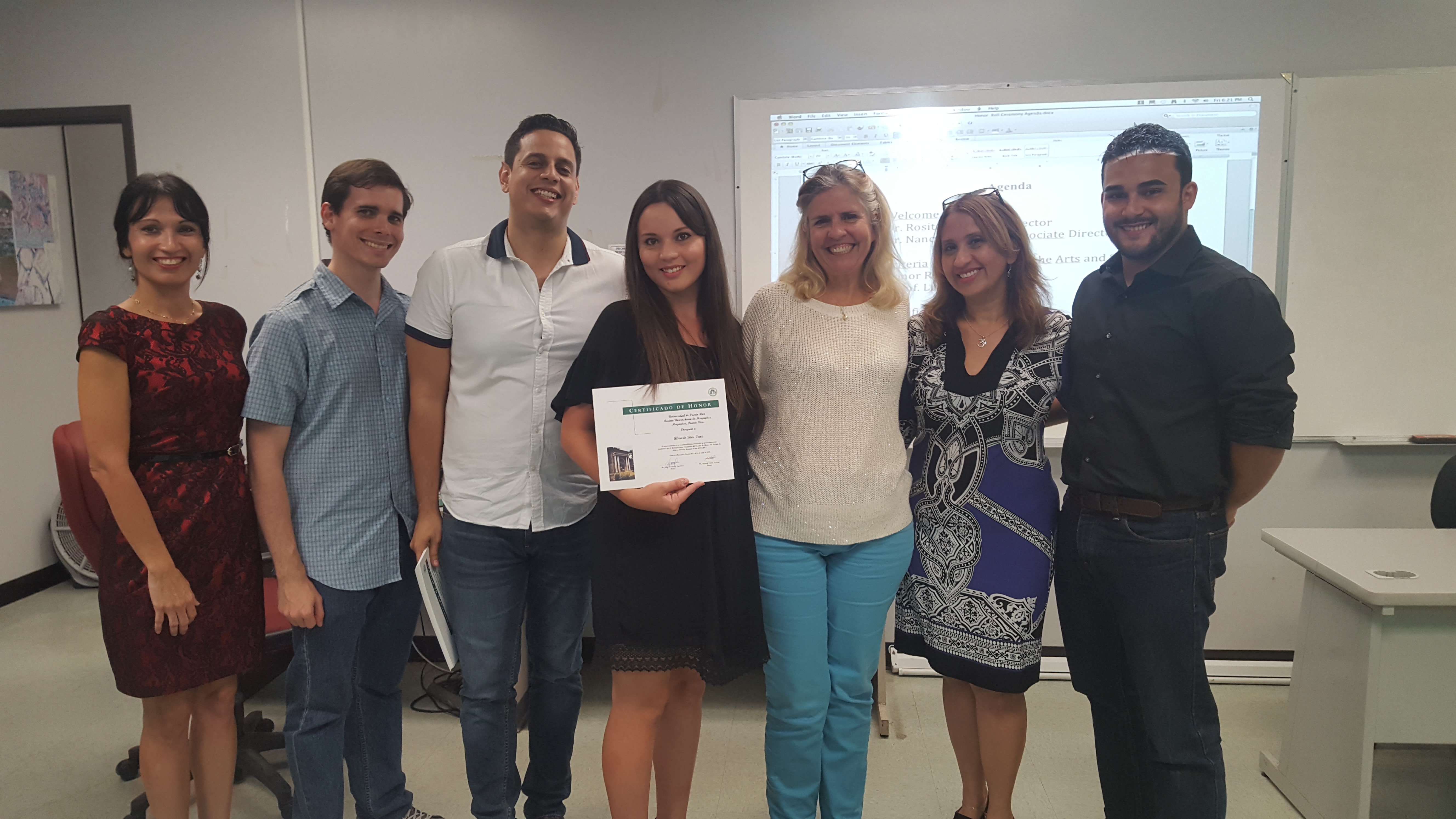 Students and professors posing for the camera at the Honor Roll Students Celebration. The student, at the middle, is holding up the certificate.