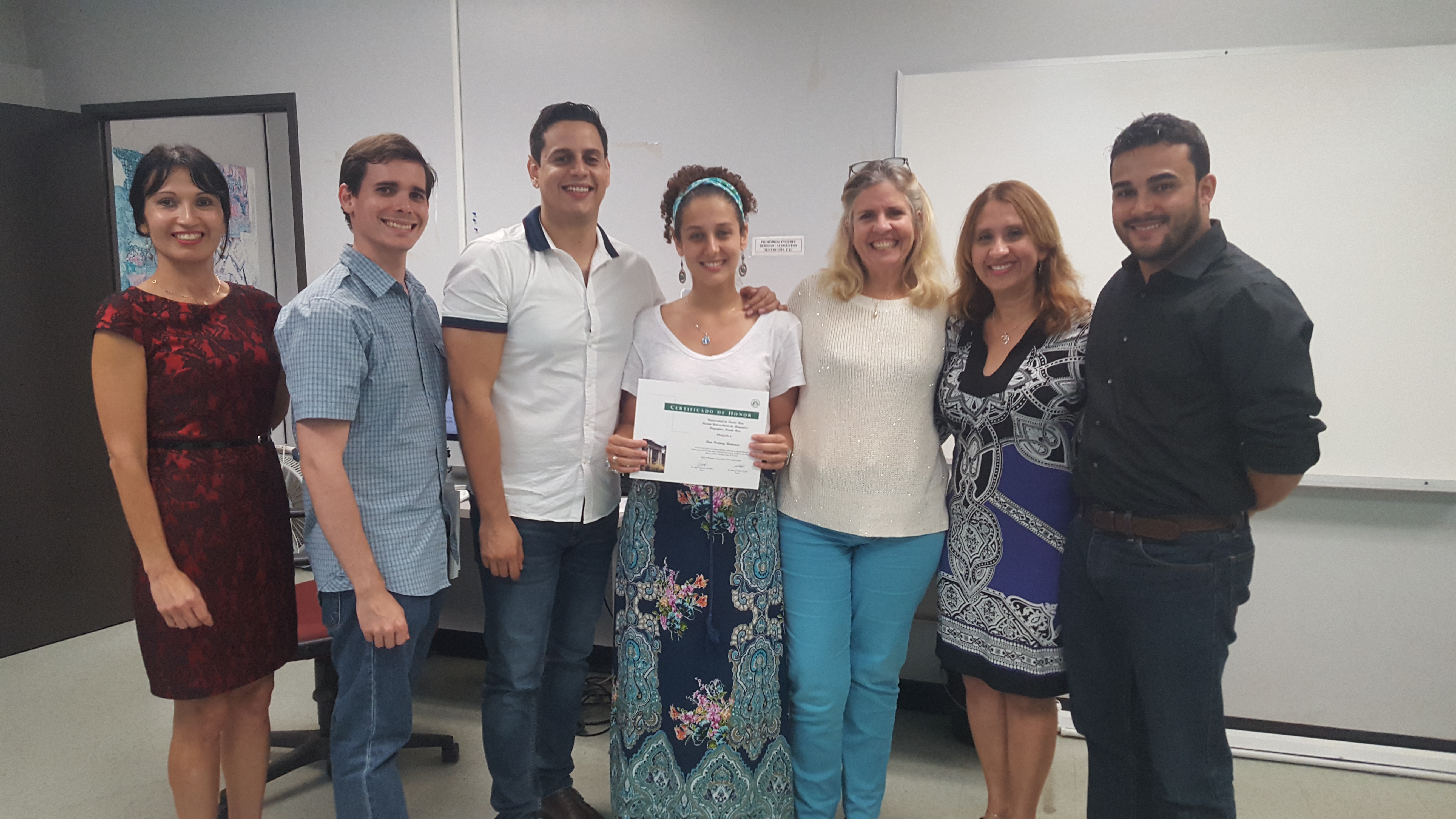 Students and professors posing for the camera at the Honor Roll Students Celebration. The student, at the middle, is holding up the certificate.