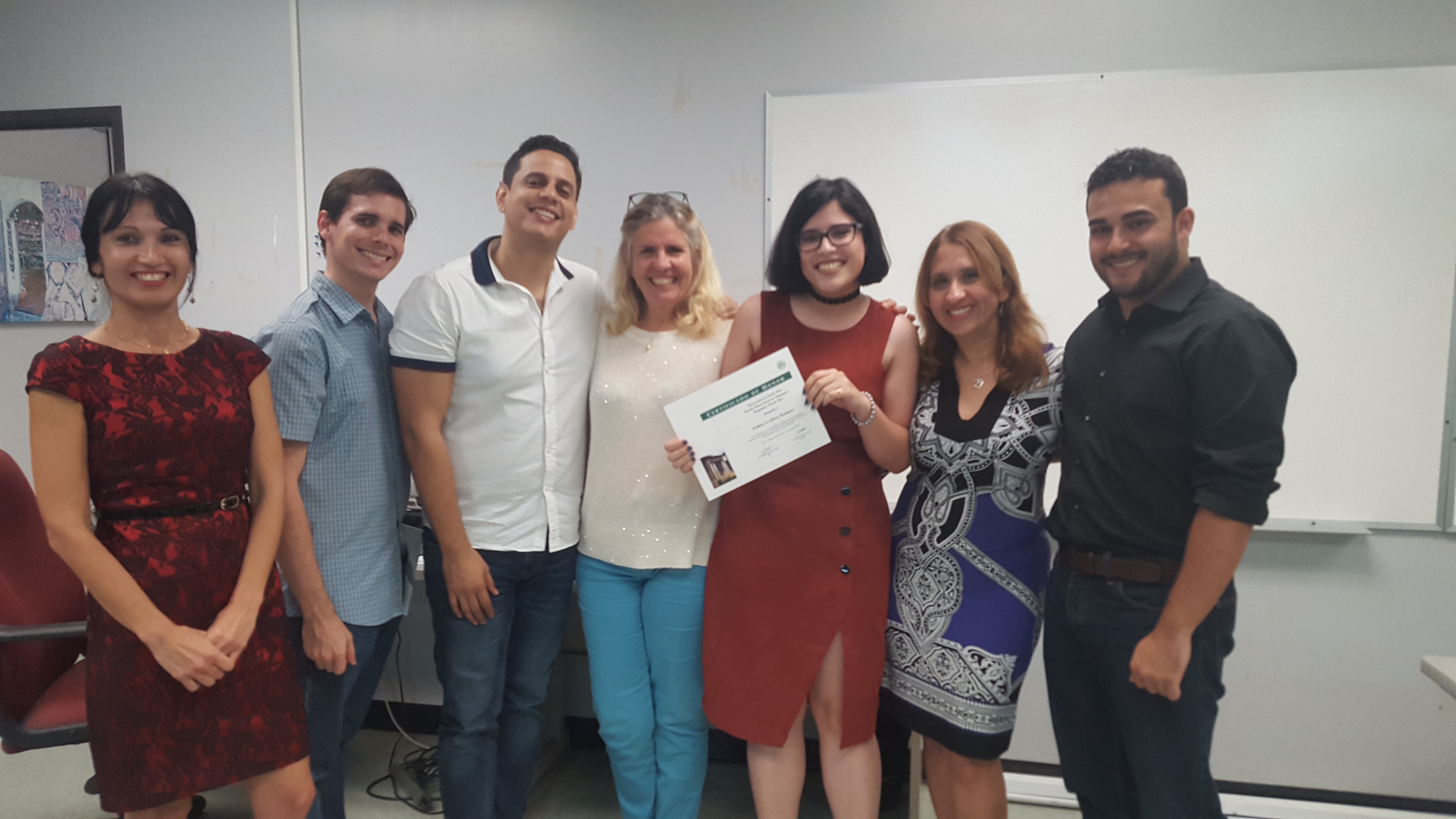 Students and professors posing for the camera at the Honor Roll Students Celebration. The student, at the middle, is holding up the certificate.