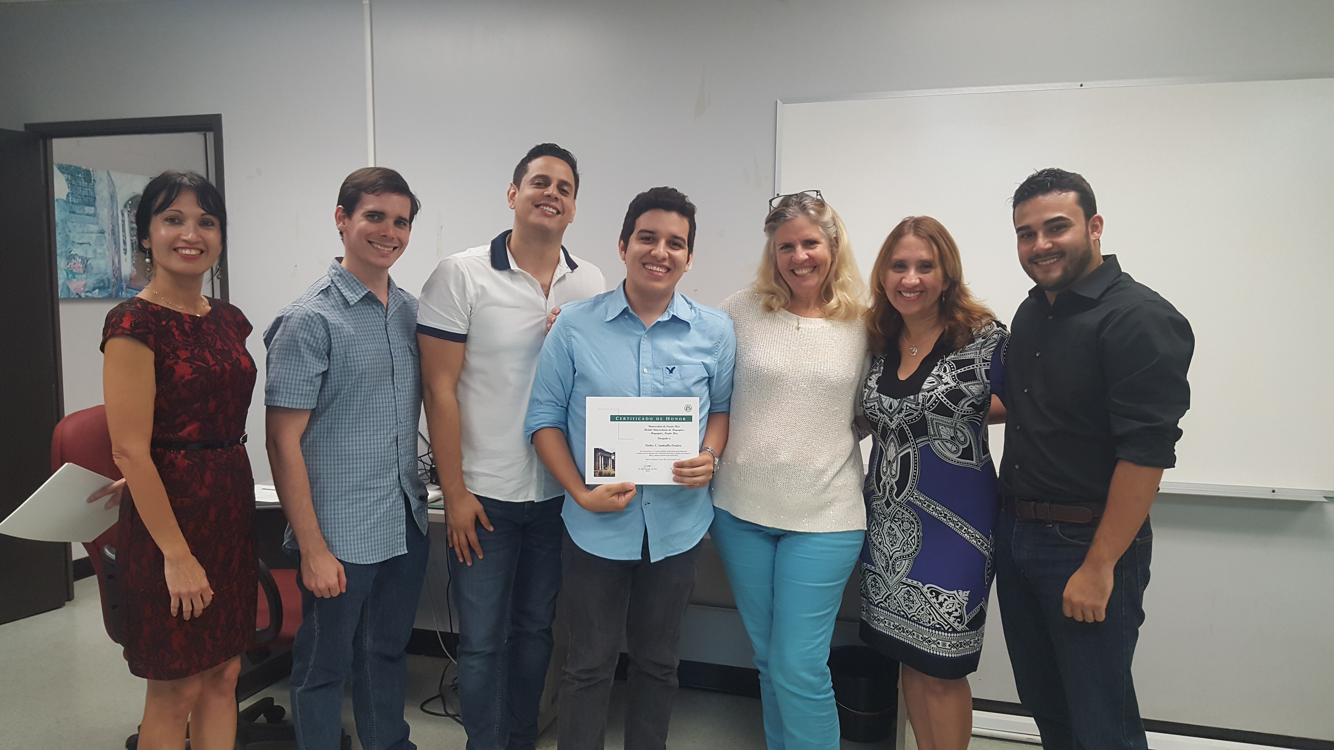 Students and professors posing for the camera at the Honor Roll Students Celebration. The student, at the middle, is holding up the certificate.