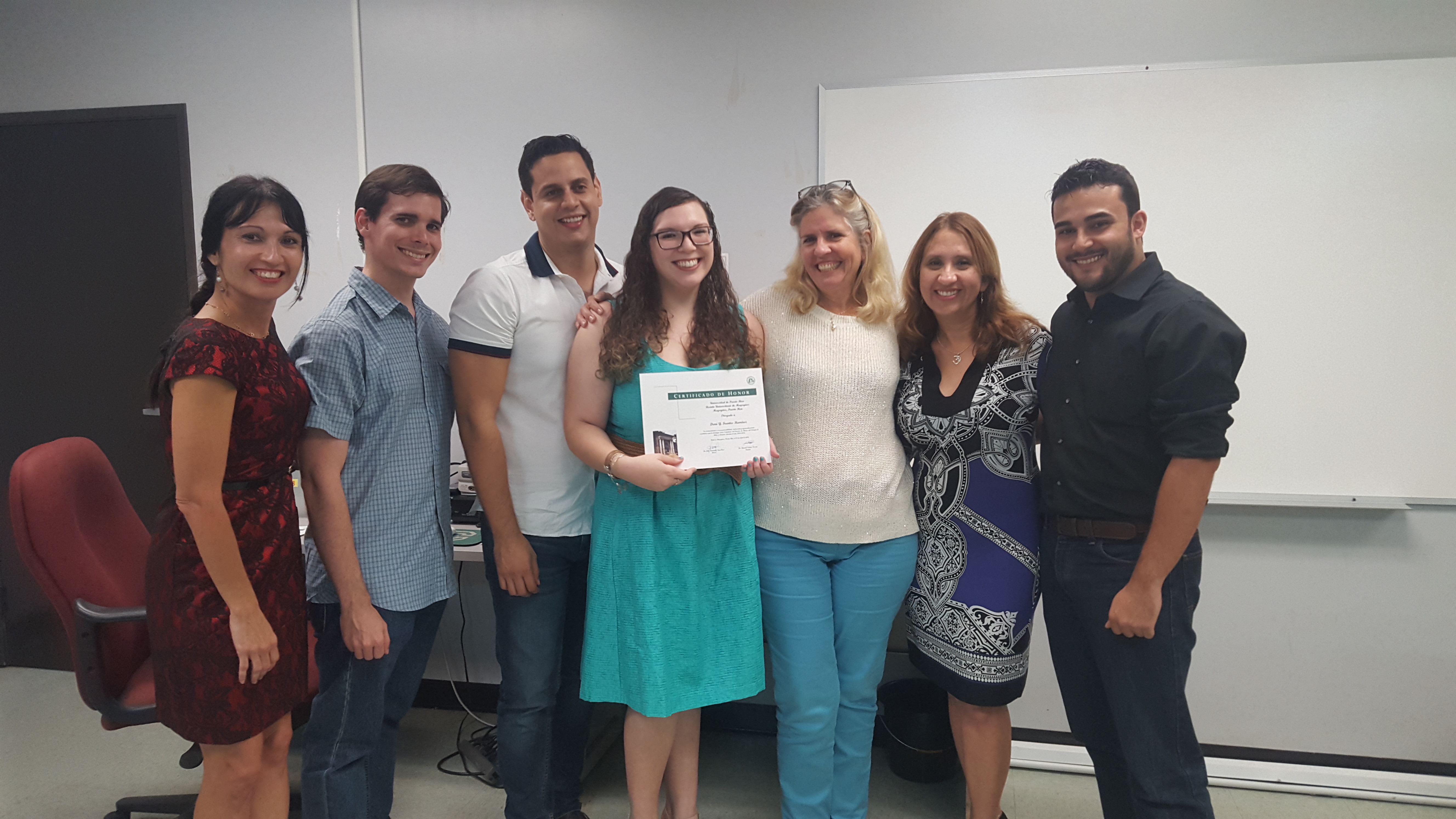 Students and professors posing for the camera at the Honor Roll Students Celebration. The student, at the middle, is holding up the certificate.