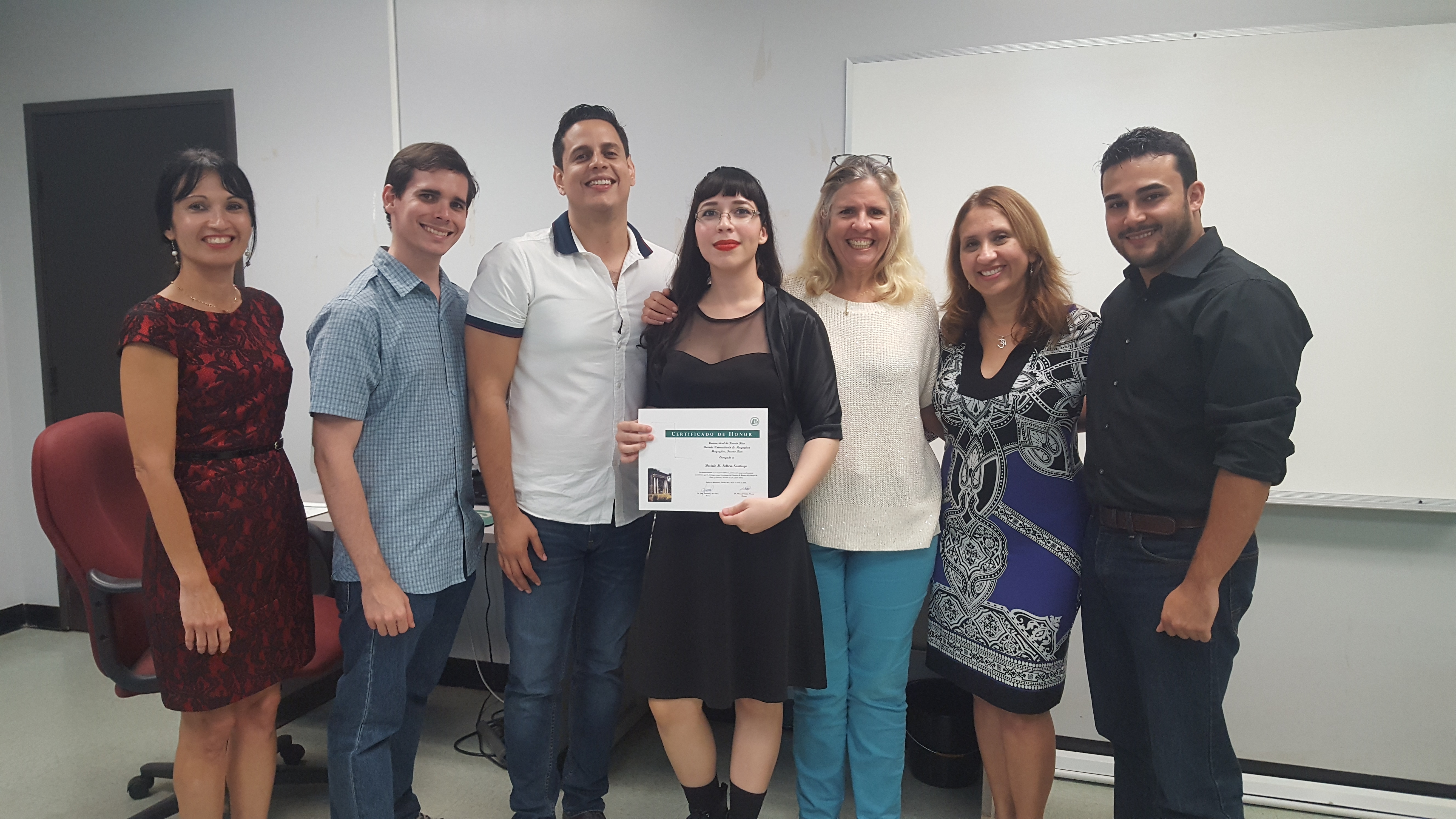 Students and professors posing for the camera at the Honor Roll Students Celebration. The student, at the middle, is holding up the certificate.