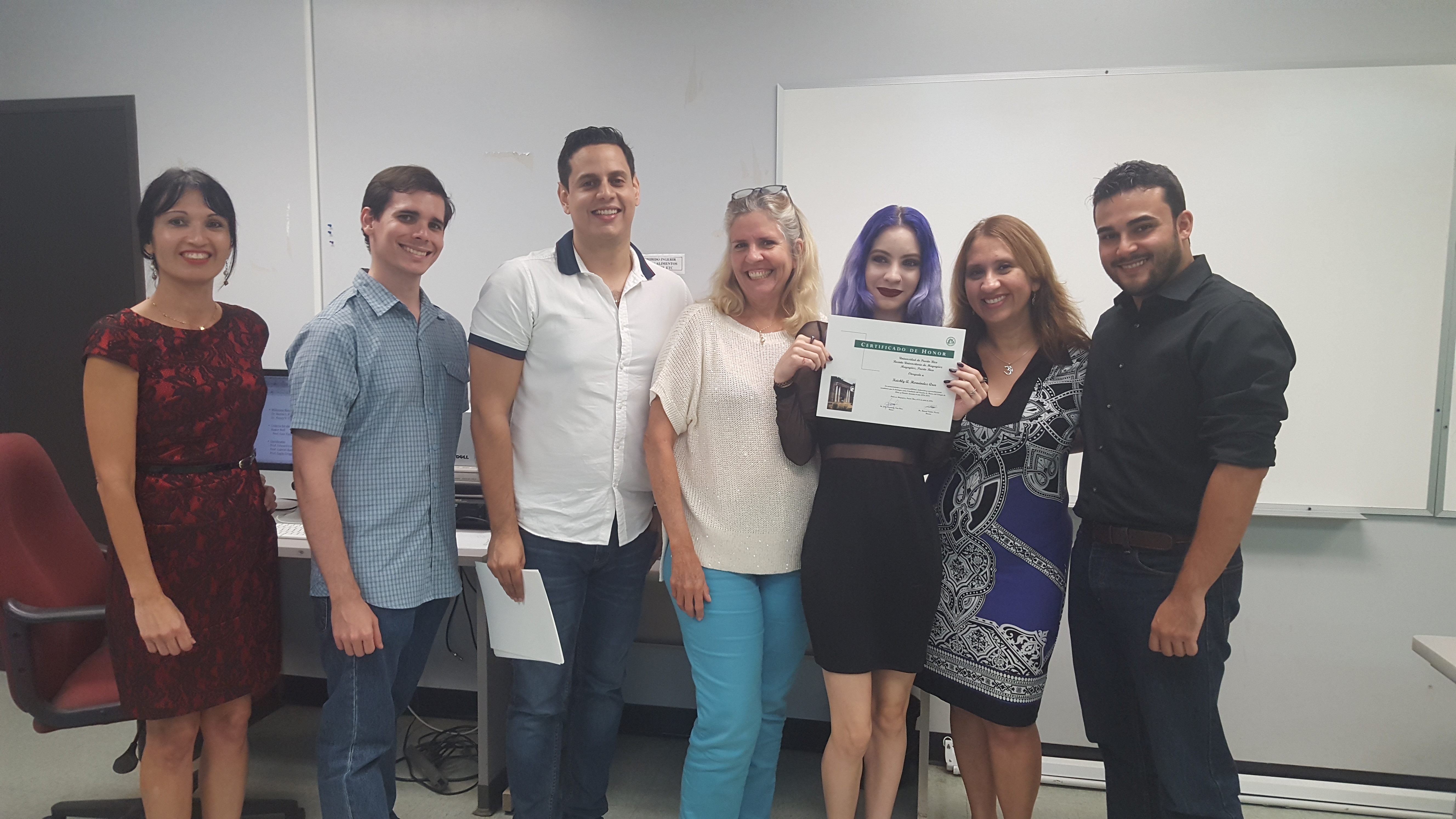 Students and professors posing for the camera at the Honor Roll Students Celebration. The student, at the middle, is holding up the certificate.