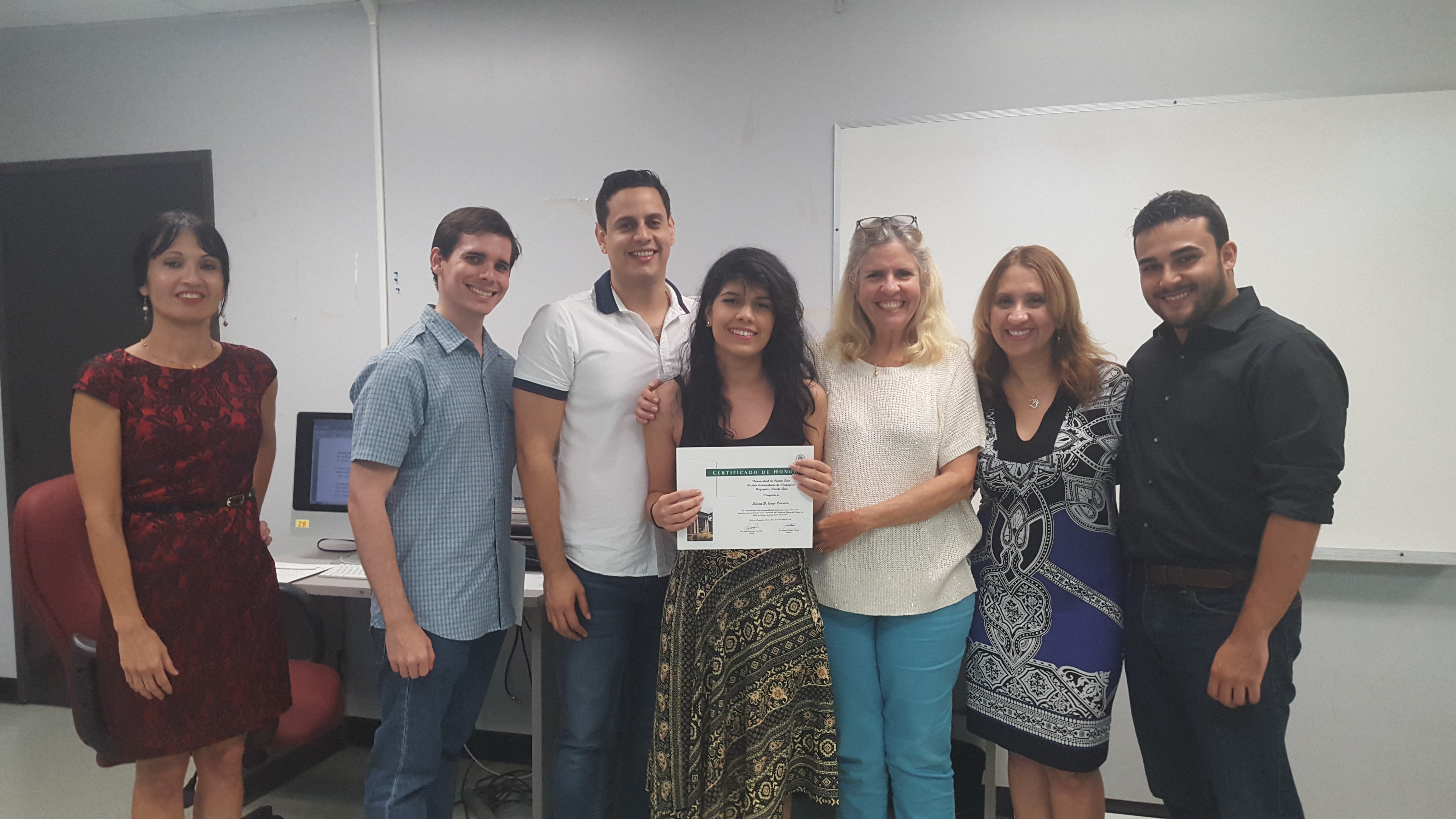 Students and professors posing for the camera at the Honor Roll Students Celebration. The student, at the middle, is holding up the certificate.