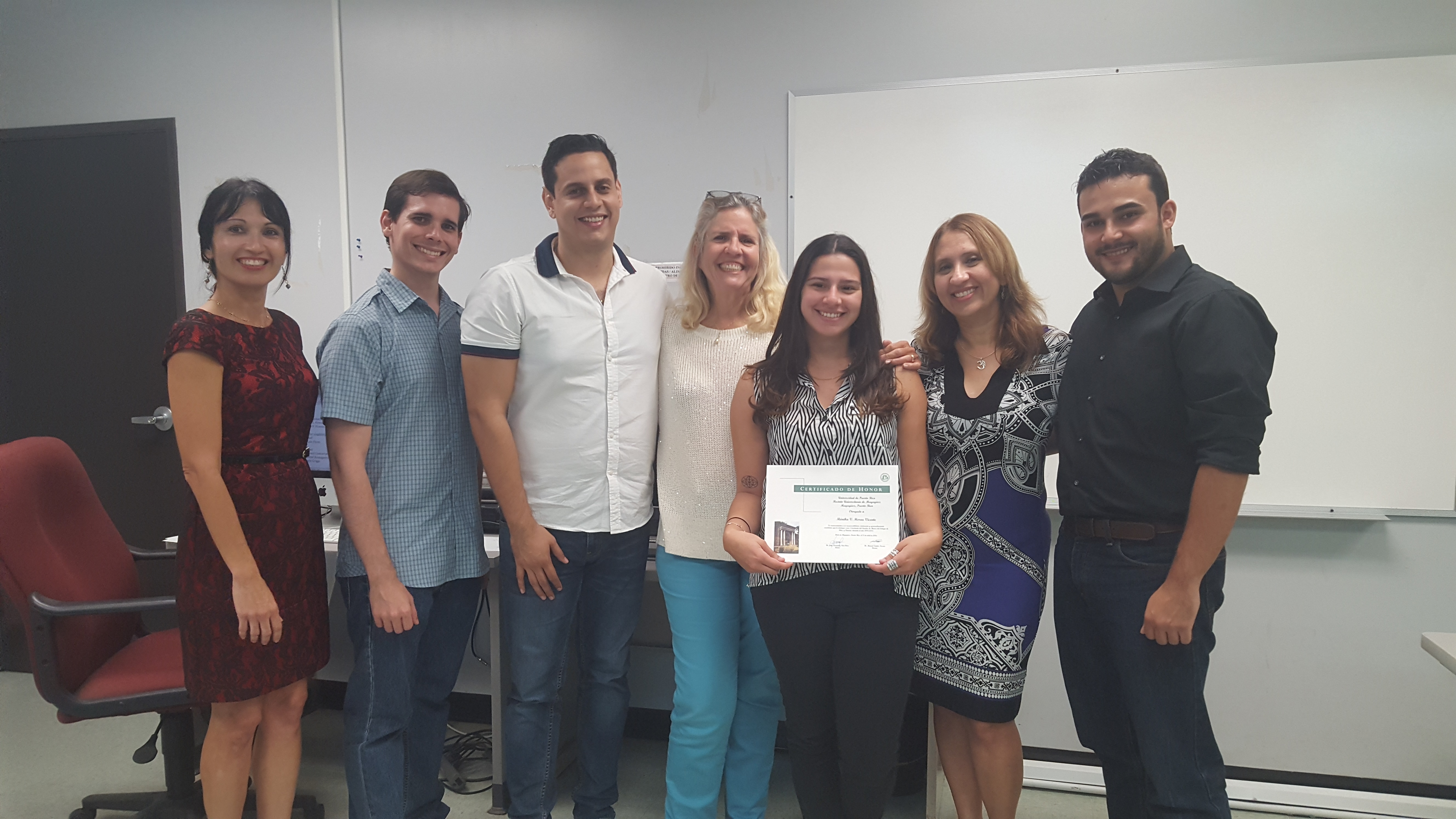 Students and professors posing for the camera at the Honor Roll Students Celebration. The student, at the middle, is holding up the certificate.