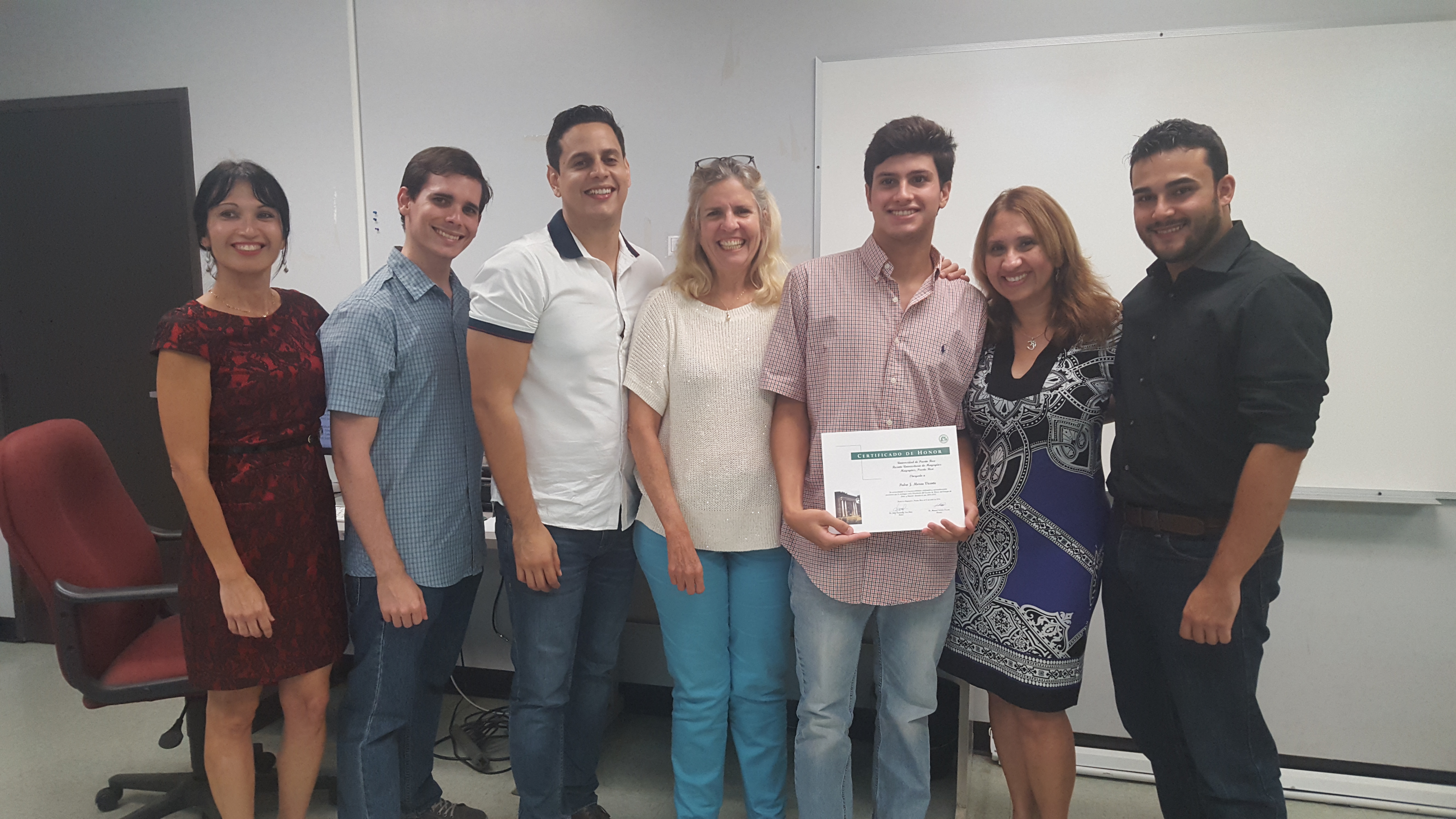 Students and professors posing for the camera at the Honor Roll Students Celebration. The student, at the middle, is holding up the certificate.