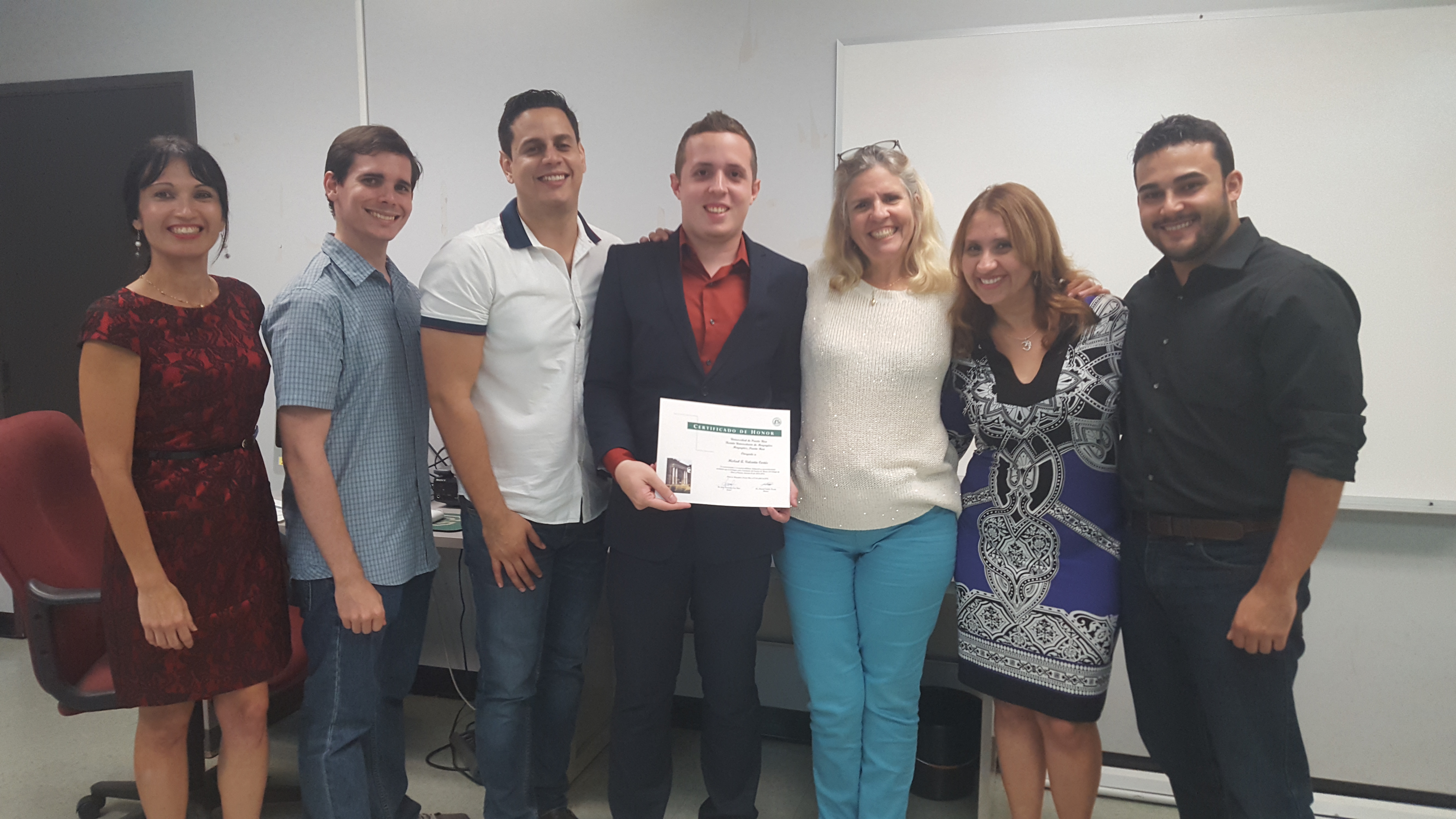 Students and professors posing for the camera at the Honor Roll Students Celebration. The student, at the middle, is holding up the certificate.