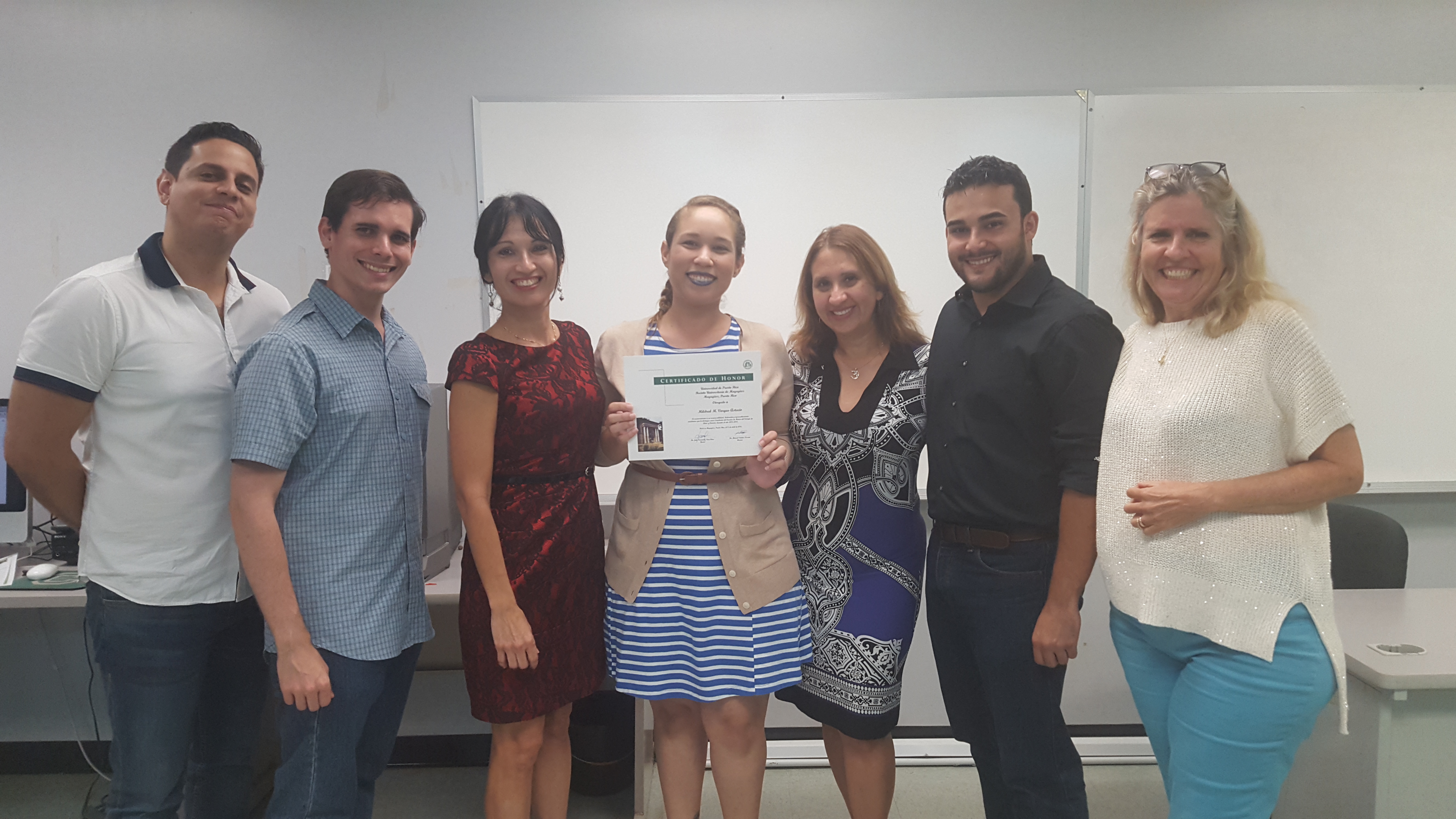 Students and professors posing for the camera at the Honor Roll Students Celebration. The student, at the middle, is holding up the certificate.