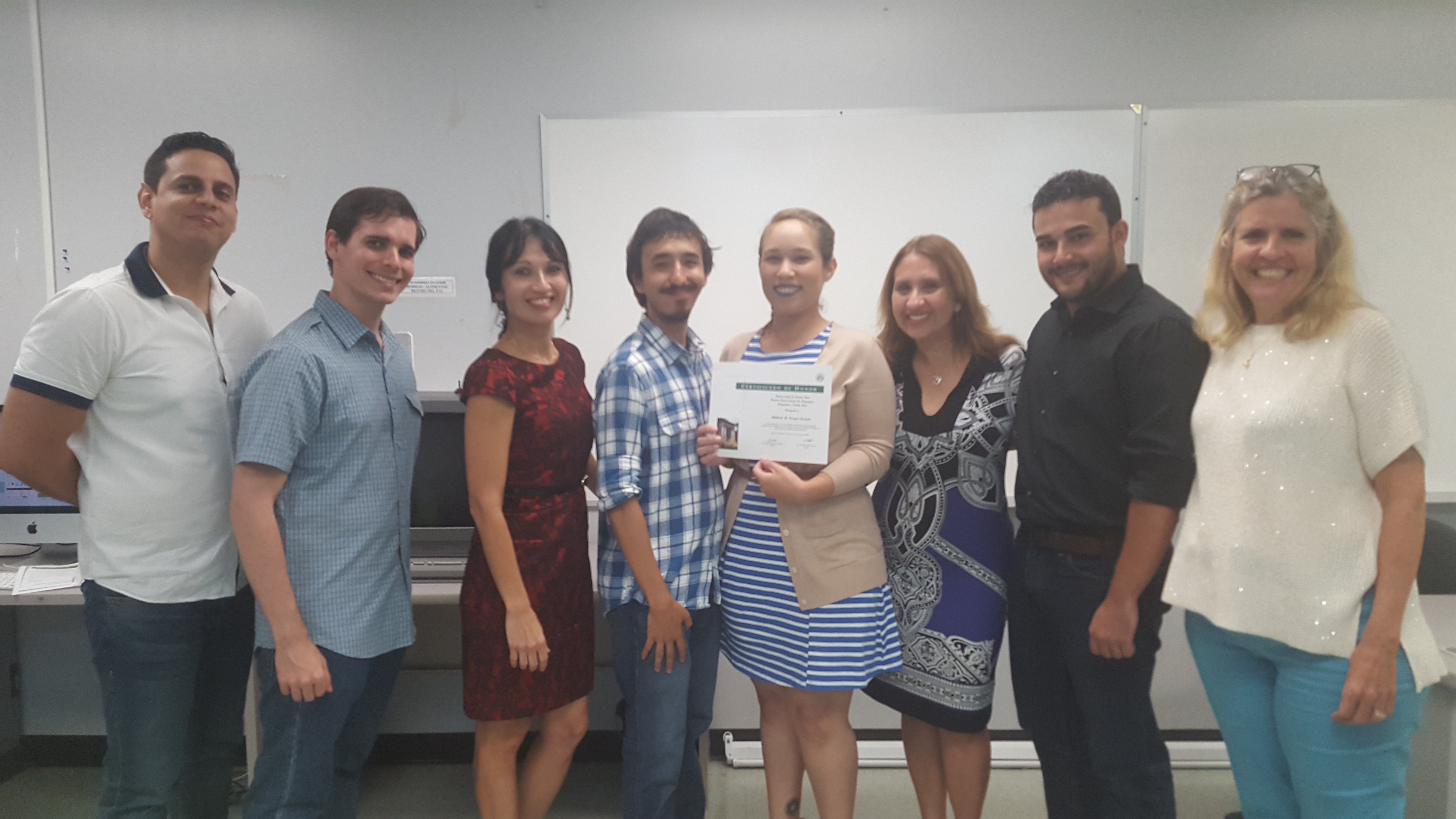 Students and professors posing for the camera at the Honor Roll Students Celebration. The student, at the middle, is holding up the certificate.