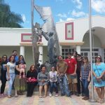 Students sitting in front of a Eugenio Maria de Hostos sculpture, posing for the camera.