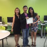 A student is posing for the camera, holding up a certificate, standing in the middle, accompanied by Nancy Vicente (left) and Rosita Rivera (right).