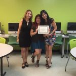 A student is posing for the camera, holding up a certificate, standing in the middle, accompanied by Nancy Vicente (left) and Rosita Rivera (right).