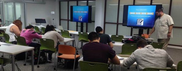 Several students are sitting by tables while working diligently on their papers.