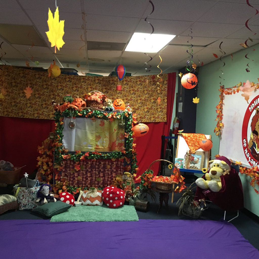 Decorations at the Children's Library Puppet Show. The puppet stage is at the center with several Halloween Themed decorations such as fall colored leaves and carved pumpkins.