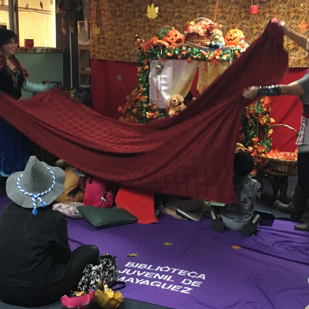 Children are being playfully covered with a blanket at the Children's Library Puppet Show.