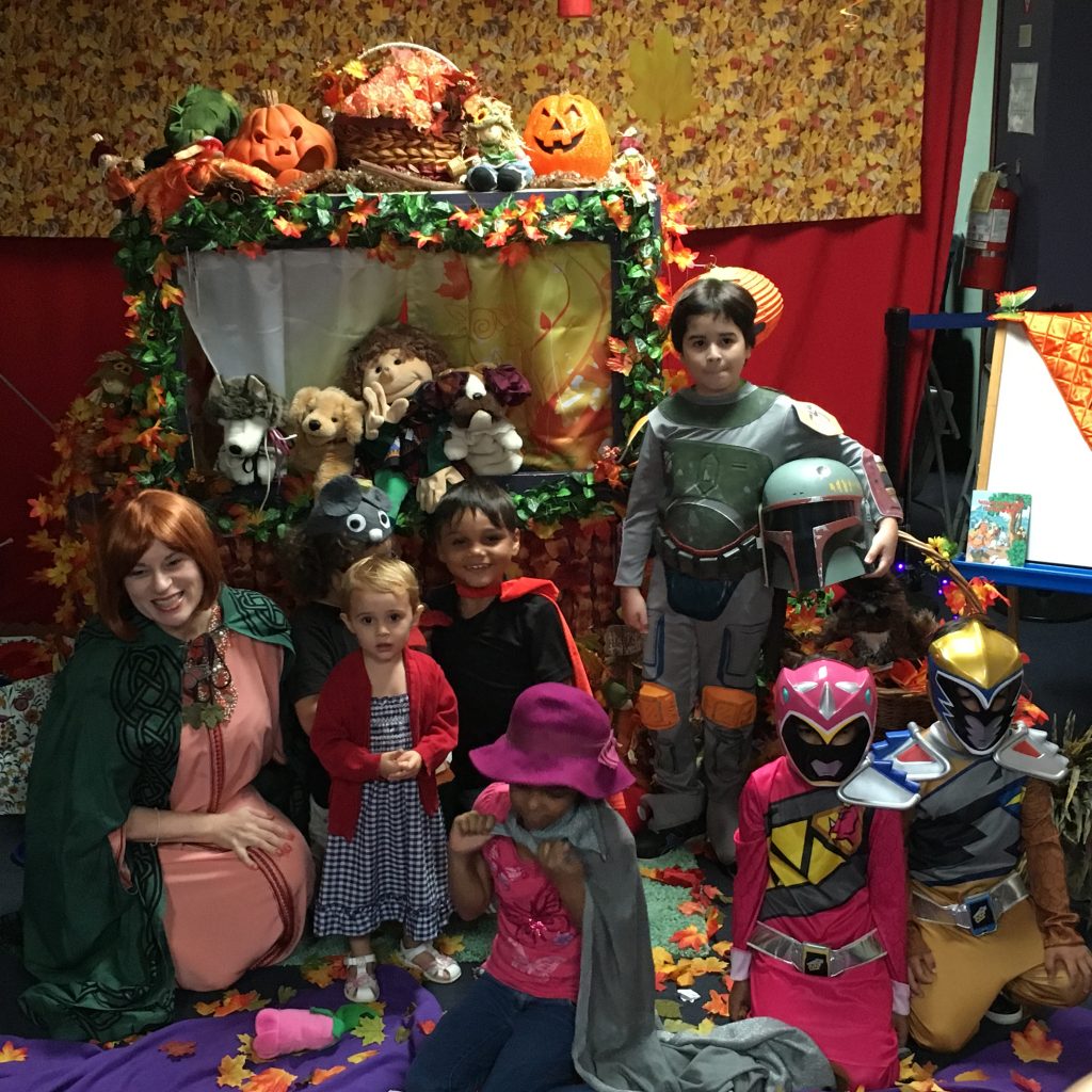 Children are posing for the camera in costume next to the Halloween Theme decorated puppet stage.