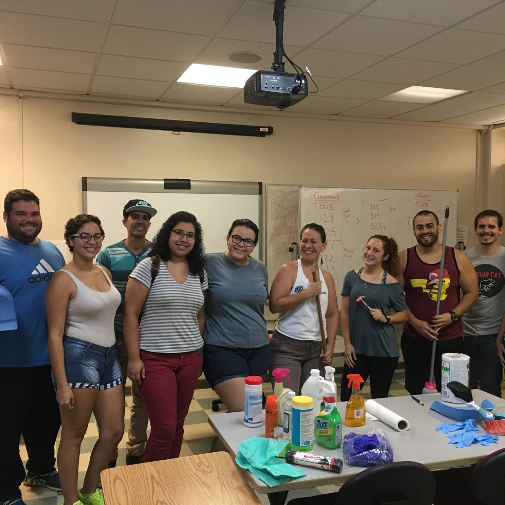 English Department's students with Mary Sefranek posing in a classroom around cleaning supplies.