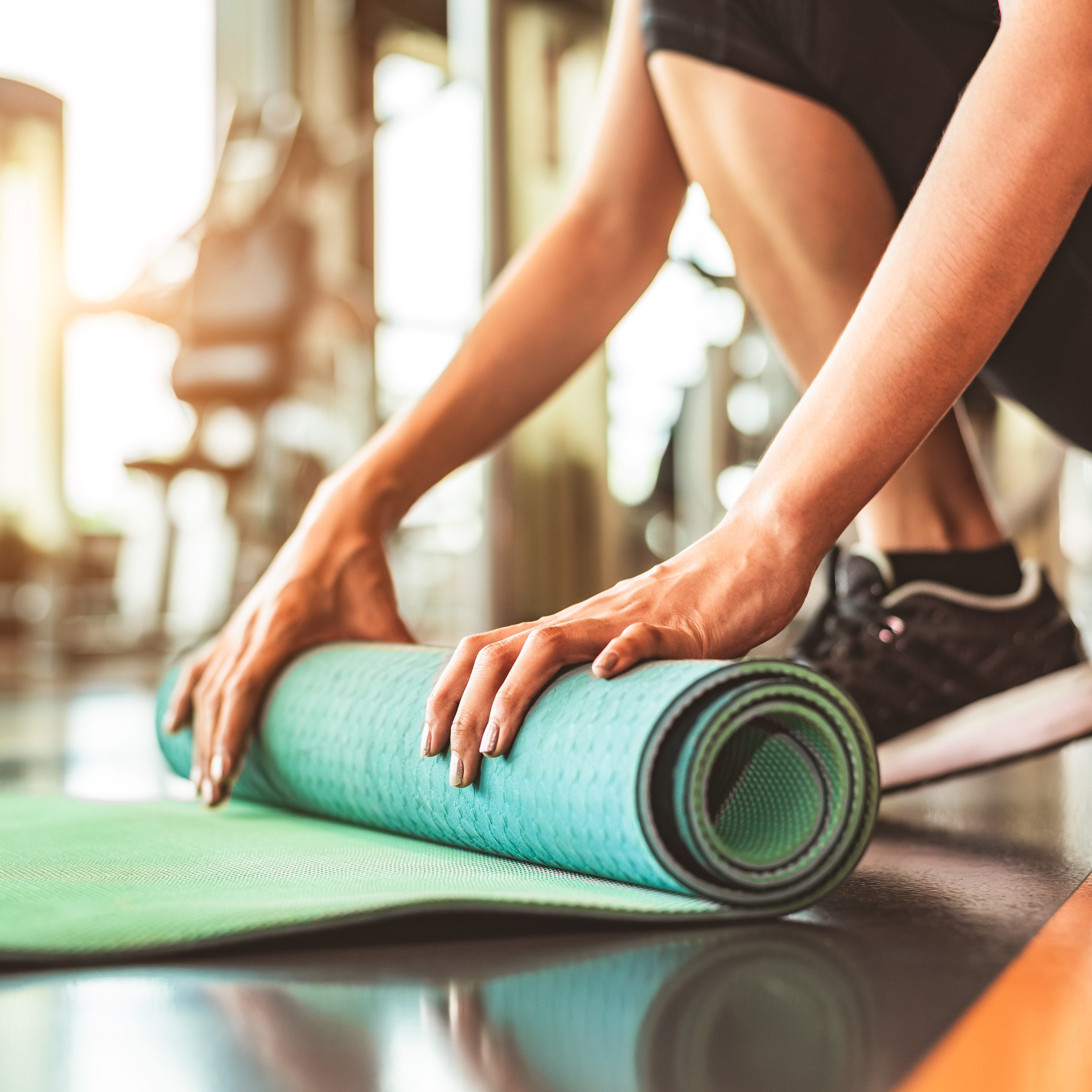 Close up of sporty woman folding yoga mattress in sport fitness gym training center background. Exercise mat rolling keeping after yoga class. Workout and sport training concept. Hands on carpet