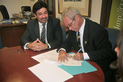 El rector del RUM, doctor Miguel A. Muñoz Muñoz (derecha) mientras firma el acuerdo colaborativo. Observa Hipólito Pérez, presidente de Cine Coop.