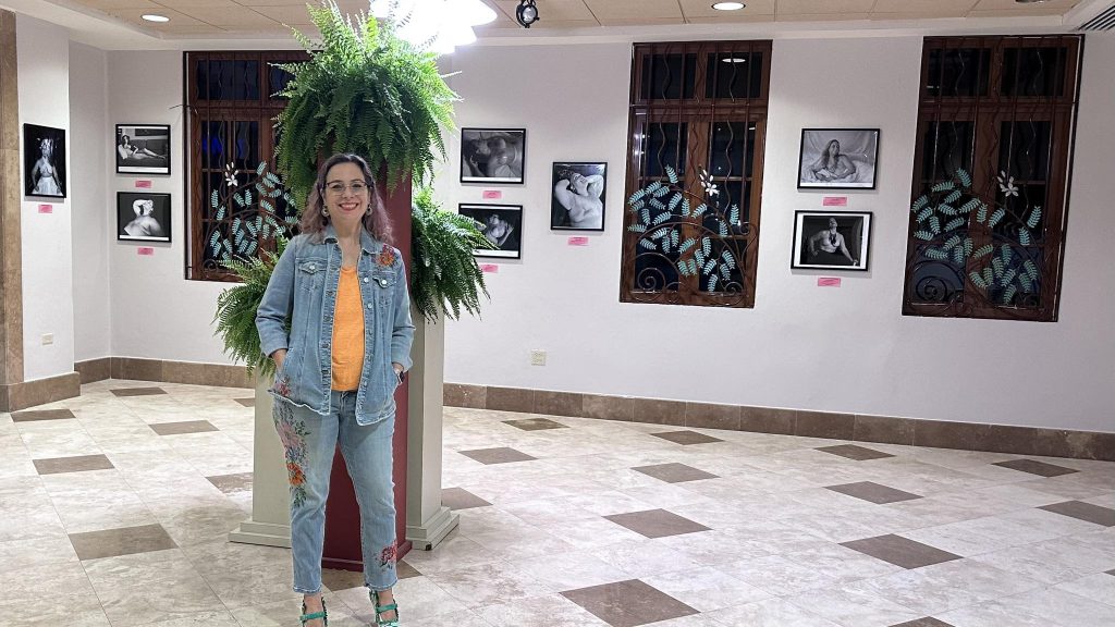 La artista visual Susan M. Olivera Alonso, egresada del Recinto Universitario de Mayagüez (RUM), durante la apertura de la exposición Cicatrices del alma en la sala de exhibiciones del Municipio de Aguadilla. En el fondo se aprecial algunas de sus obras que son fotos de féminas que han tenido mastectomías por cáncer de seno.