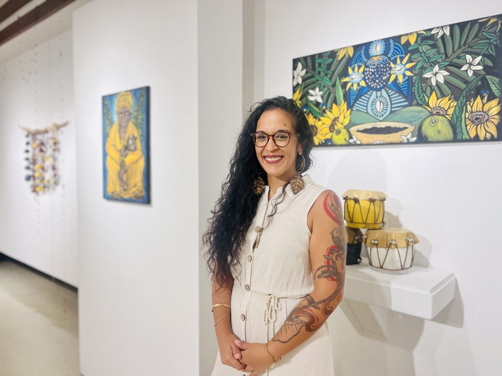 La artista mayagüezana Bárbara W. Pérez Rodríguez, egresada colegial, frente a sus obras en la Galería de Arte del RUM.