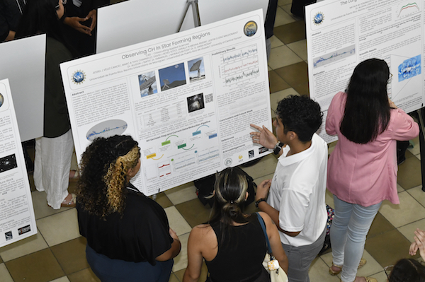 Foto desde arriba de un grupo de estudiantes frente a uno de los afiches de investigación.