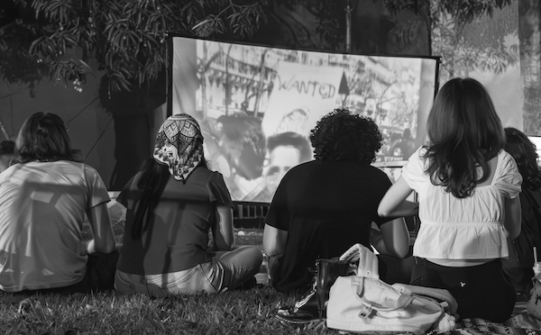 Grupo de estudiantes observa película proyectada en pantalla en el patio del edificio Chardón.