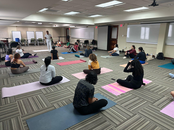 Grupo de estudiantes sentado en el piso, toman la clase de yoga con el doctor Emir Rivera.