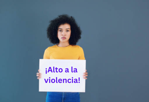 Una mujer sostiene un letrero que lee Alto a la violencia. De pie, con pared de fondo azul.