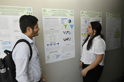 Dos estudiantes presentan sus afiches durante la reciente Feria de Investigación y Diseño de Ingeniería Industrial.