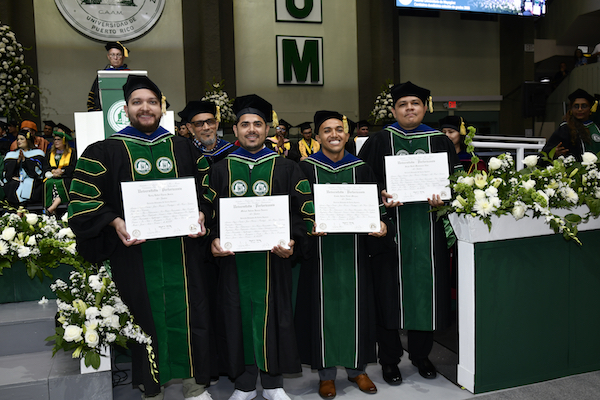 Cuatro estudiantes de Ingeniería Eléctrica que recibieron su doctorado, de pie frente al escenario, con sus diplomas en mano.