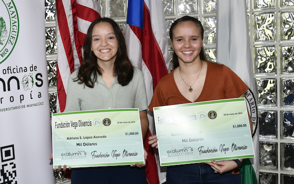 Las colegiales Adriana S. López Acevedo y Kiarelis López Soto, ambas del Departamento de Química del RUM, recibieron la beca de la Fundación Vega Olivencia. De pie, sostienen cheque simbólico. Al fondo, las banderas del Colegio, Puerto Rico y Estados Unidos.