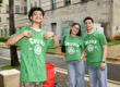 Tres estudiantes de nuevo ingreso posan para la cámara con sus camisetas verdes que dicen Colegio junto al emblema institucional.