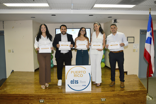 Grupo de egresados de la cuarta cohorte del Programa Internacional para la Gestión del Deporte en el RUM, de pie en el podio del anfiteatro de Empresas, sostienen sus certificados.