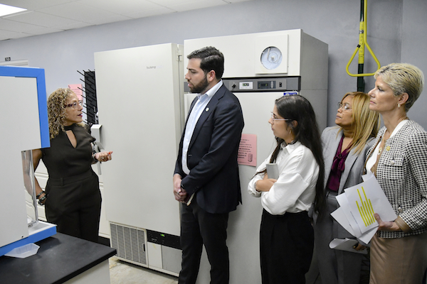 El secretario del Departamento de Desarrollo Económico y Comercio, Sebastián Negrón Reichard, durante su visita al Recinto Universitario de Mayagüez, en uno de los laboratorios del CITAI, de pie junto a funcionarias y docentes colegiales.