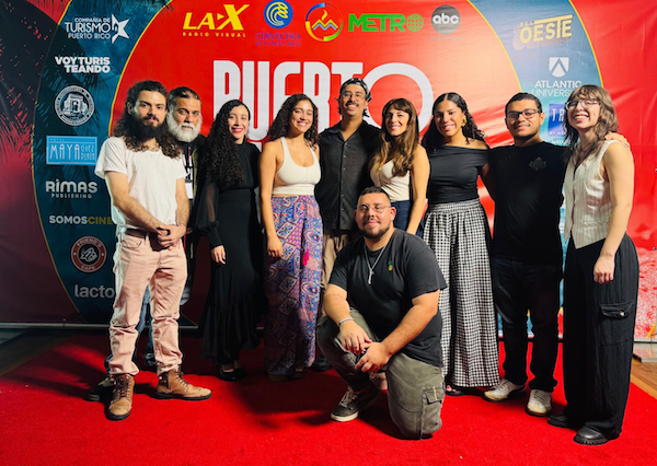 Grupo de estudiantes y exalumnos del Certificado en Cine del Recinto Universitario de Mayagüez que se alzó con el premio a Mejor Cortometraje Estudiantil en el Puerto Rico Film Festival 2025, gracias a su producción Luz quiere un beibi. Todos de pie frente al cartel de promoción del festival.