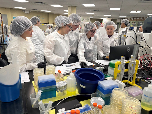 Estudiantes del RUM en un laboratorio durante el adiestramiento del programa Amgen BioTalents, con vestimenta de seguridad.