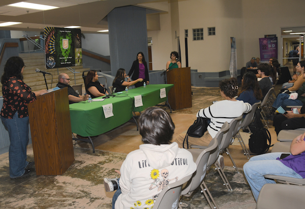 La doctora Yadira Malavez Acevedo, junto a una estudiante en el podio, durante la sesión de preguntas a los panelistas de la industria, quienes están sentados en una mesa en el vestíbulo del edificio de Biología.