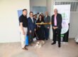 Personal docente y administrativo del Recinto Universitario de Mayagüez inaugura las instalaciones del NeuroLab MindMarket Lab en el Edificio de Empresas. Todos de pie frente a la puerta del laboratorio en el corte de cinta, con la mascota Jane.